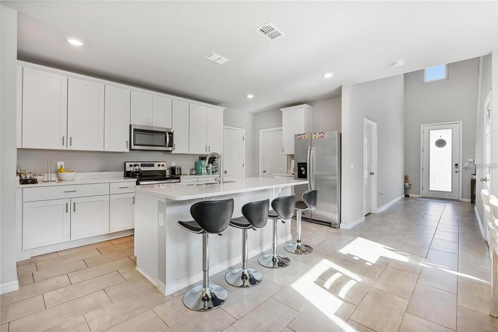 A kitchen with white cabinets, a central island with bar stools, and tile flooring — 17411 MILLION LAKES COURT, CLERMONT, FL