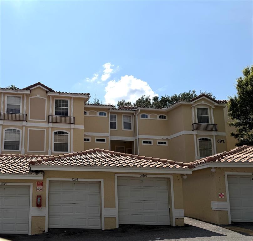 A multi-story tan apartment building features several garage doors at the ground level — 692 SEABROOK COURT UNIT 102, ALTAMONTE SPRINGS, FL