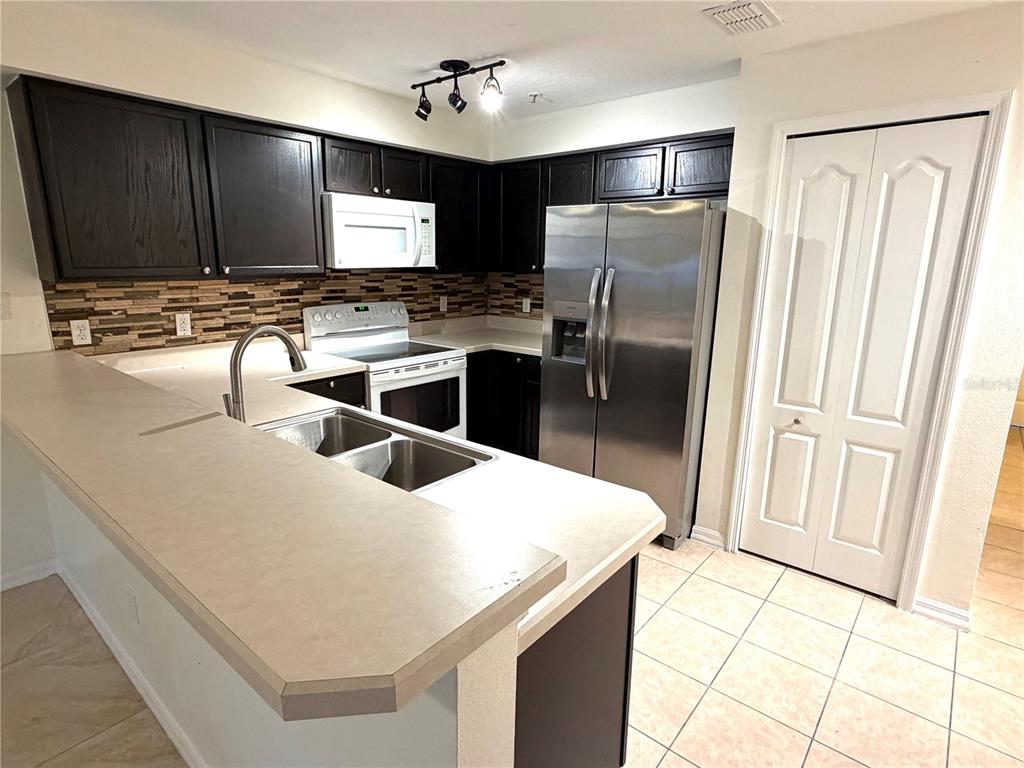 A kitchen features dark wood cabinets, stainless steel appliances, and a light-colored countertop peninsula — 692 SEABROOK COURT UNIT 102, ALTAMONTE SPRINGS, FL