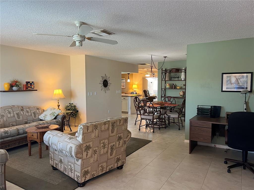 An open-concept living and dining area features tile flooring, a ceiling fan, and palm-patterned furniture — 1814 COLUMBINE PLACE, SUN CITY CENTER, FL