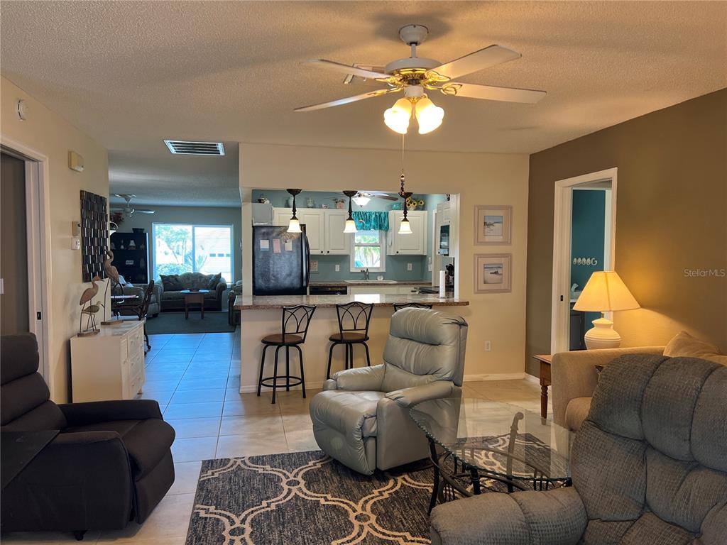 A living room with a ceiling fan, tiled floors, and an open kitchen with bar seating — 1814 COLUMBINE PLACE, SUN CITY CENTER, FL