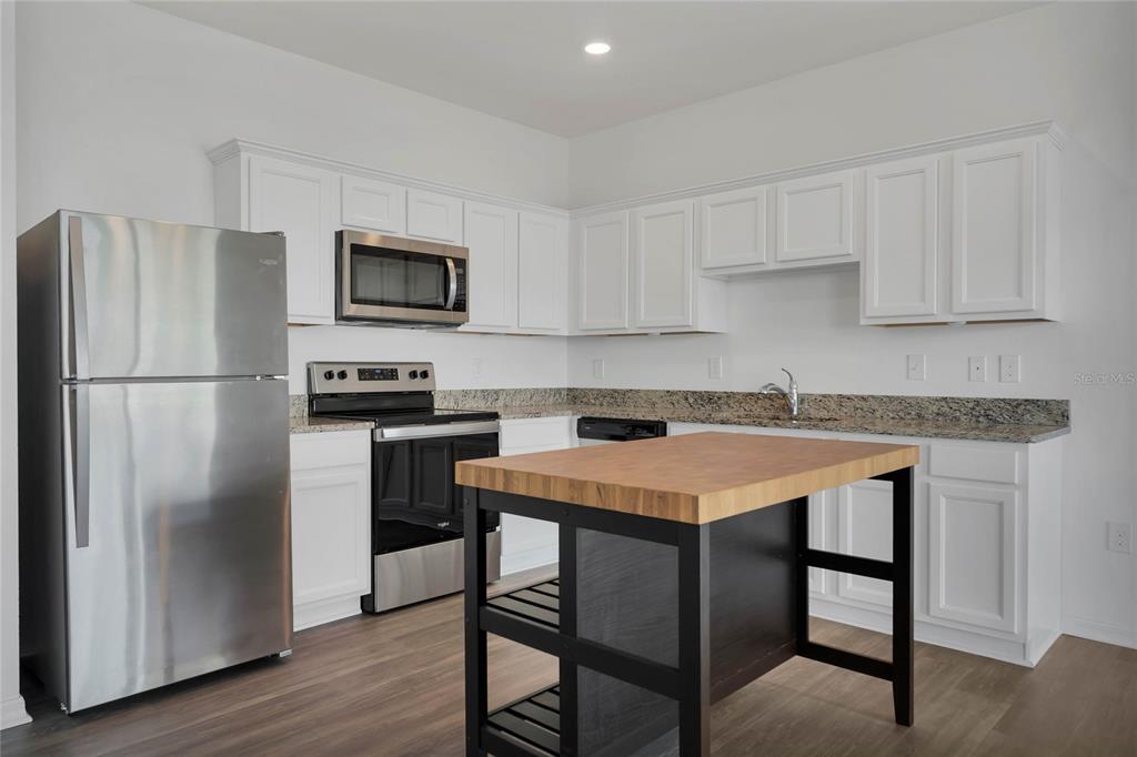 A kitchen features white cabinets, stainless steel appliances, granite countertops, and a wooden kitchen island — 840 GRANDIN STREET, DAVENPORT, FL