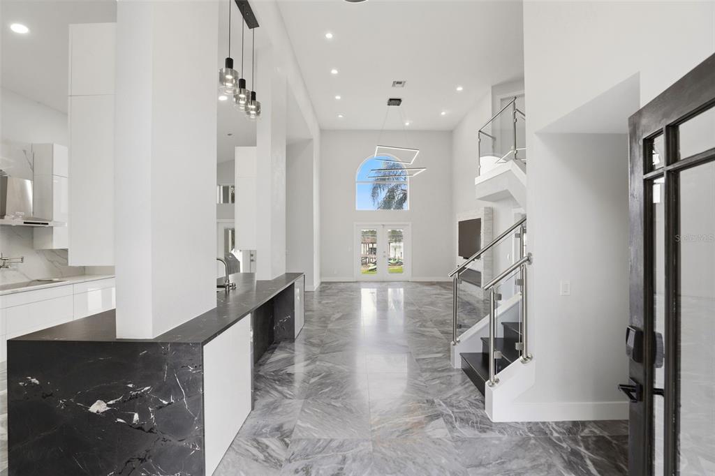 A modern open-concept living area features marble flooring, a black marble kitchen island, and stairs — 673 LAKE HARBOR CIRCLE, ORLANDO, FL