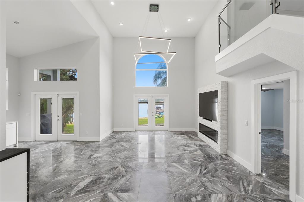 A spacious living room features high ceilings, marble tile flooring, a fireplace, and glass doors — 673 LAKE HARBOR CIRCLE, ORLANDO, FL