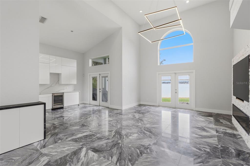 A bright living room features high ceilings, marble flooring, a modern chandelier, and lake views — 673 LAKE HARBOR CIRCLE, ORLANDO, FL