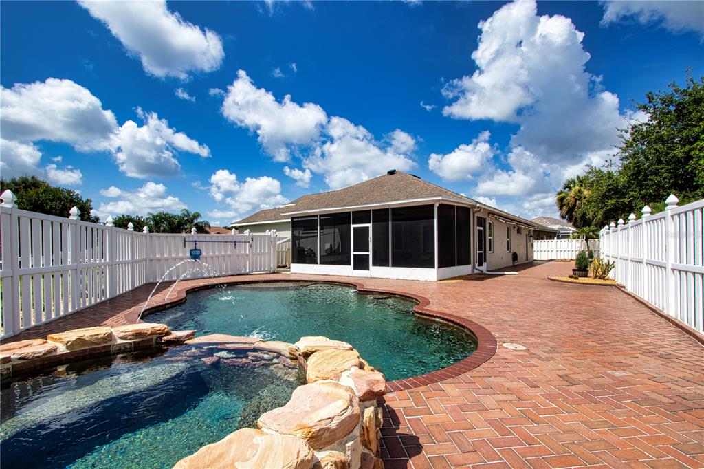 A backyard features a swimming pool with a rock-lined spa, brick pavers, and white fencing — 515 PLANTERS MANOR WAY, BRADENTON, FL