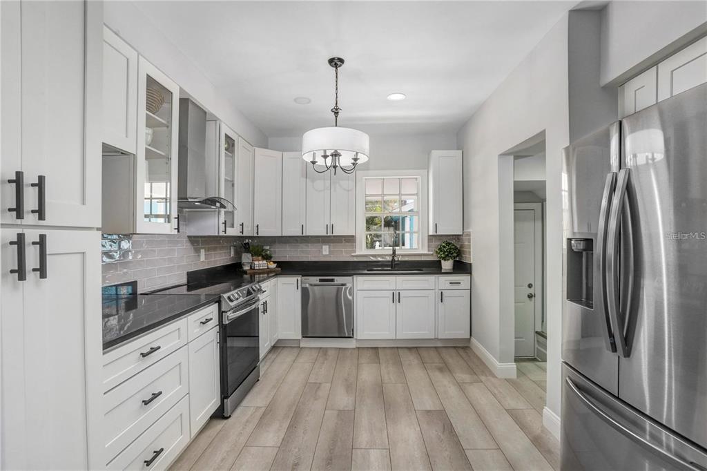 A modern kitchen features white cabinets, black countertops, stainless steel appliances, and wood-look tile flooring — 1960 MCKINLEY STREET, CLEARWATER, FL