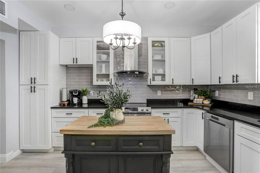 A kitchen features white cabinets, a dark island with a wood top, and gray backsplash tile — 1960 MCKINLEY STREET, CLEARWATER, FL