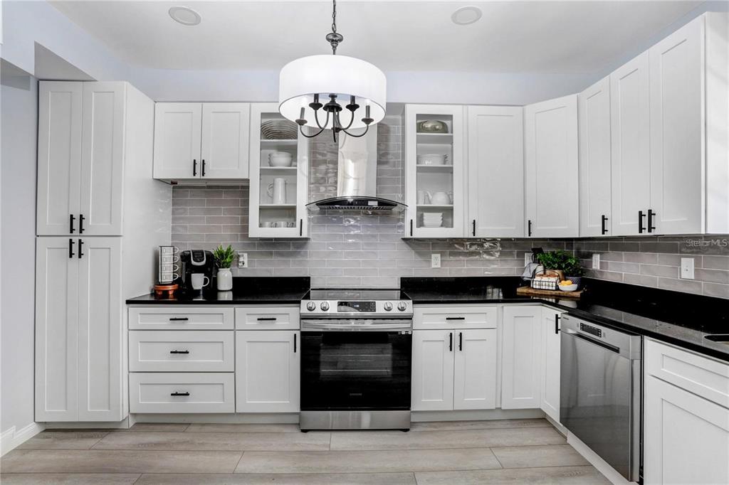 A kitchen features white shaker cabinets, black countertops, stainless steel appliances, and gray subway tile — 1960 MCKINLEY STREET, CLEARWATER, FL