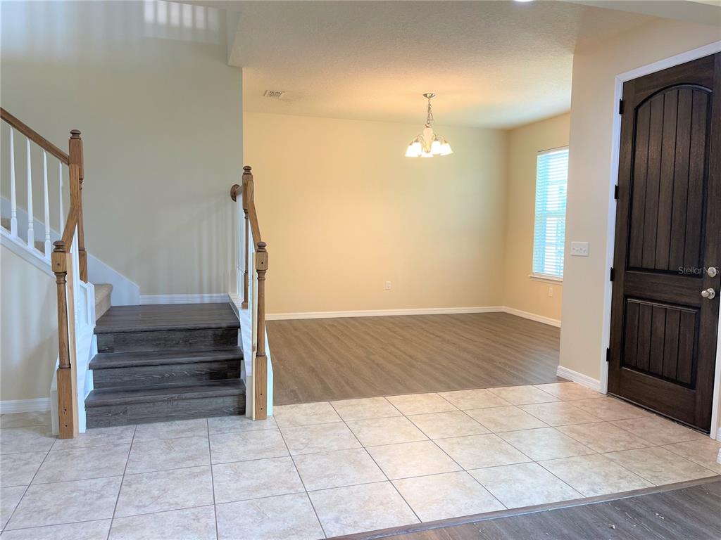An entryway with tiled floors, a wooden staircase, and an adjacent room with wood flooring — 8415 MOREHOUSE DRIVE, ORLANDO, FL
