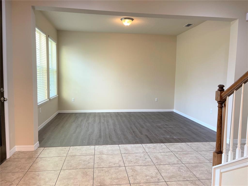 An empty room features gray wood-look flooring, beige walls, two windows, and a ceiling light — 8415 MOREHOUSE DRIVE, ORLANDO, FL