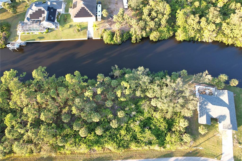 An aerial view shows a wooded lot situated between a canal and a residential street — 1100 MARCH DRIVE, PORT CHARLOTTE, FL