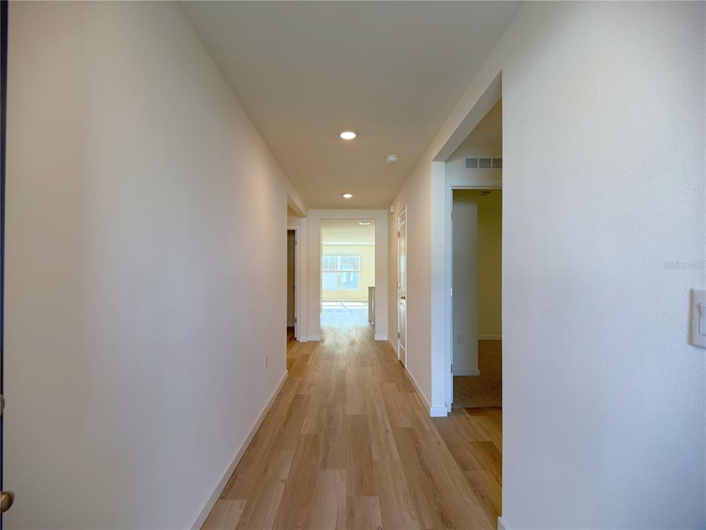 A hallway with light wood-look flooring leads toward a bright room with a window — 7214 SE 112TH LANE, BELLEVIEW, FL