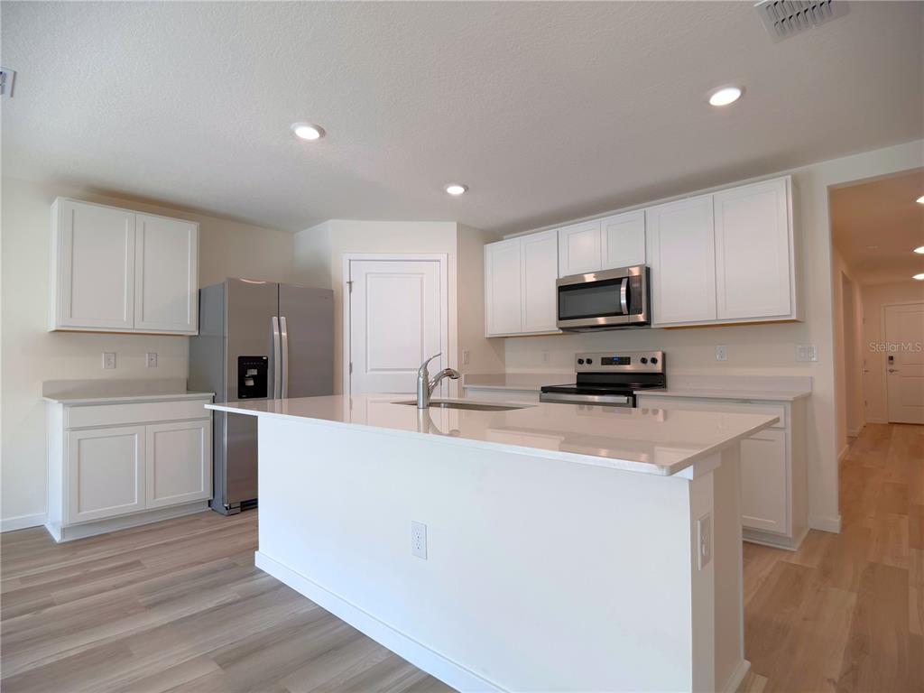 A kitchen features white cabinets, stainless steel appliances, a center island, and light wood flooring — 7214 SE 112TH LANE, BELLEVIEW, FL
