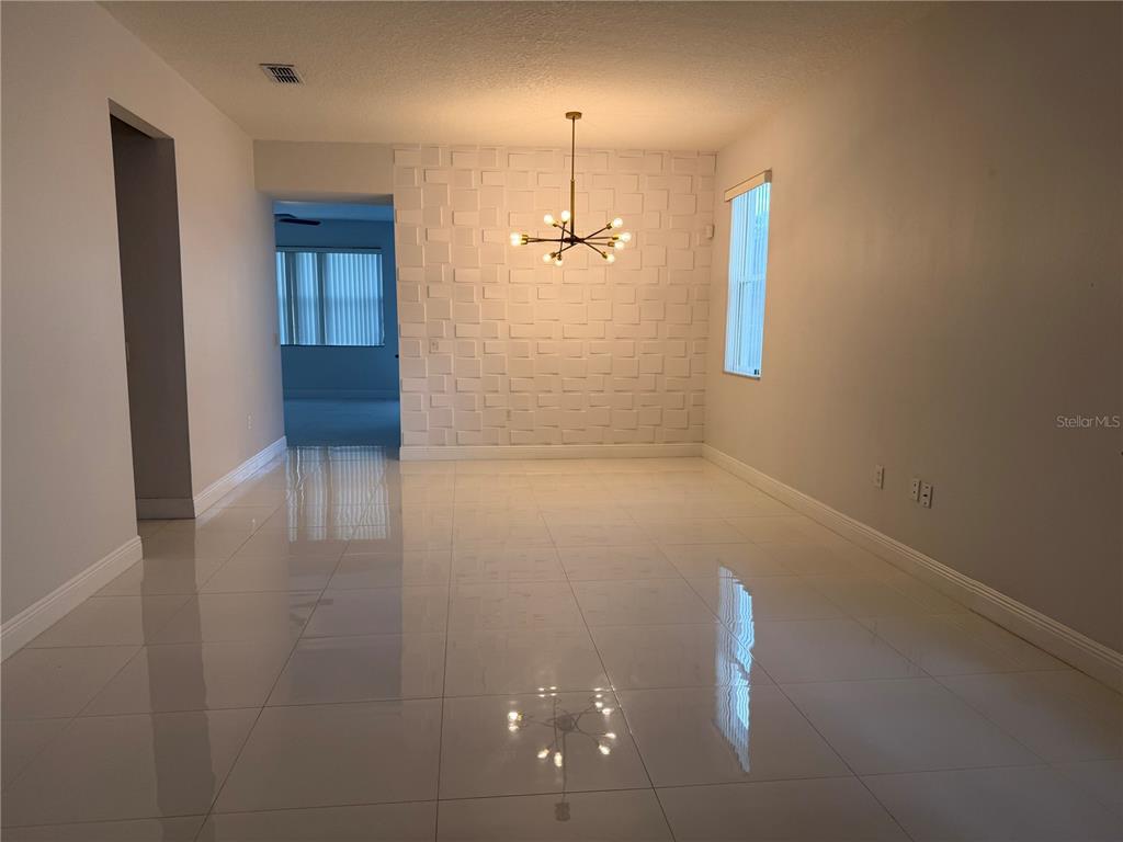 A dining room with white tile floors, a textured accent wall, and a modern chandelier — 1112 PINE RIDGE DRIVE, DAVENPORT, FL