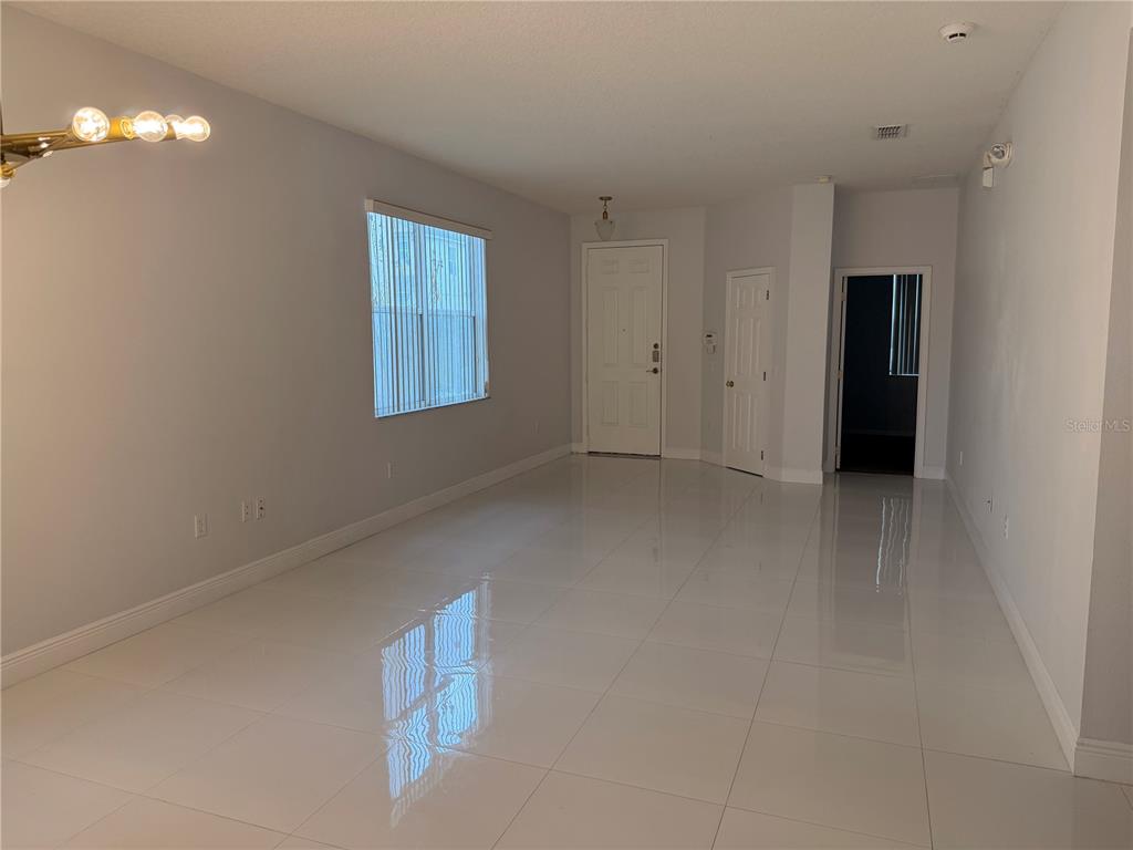 An empty room with white tile flooring, a window with blinds, and a white door — 1112 PINE RIDGE DRIVE, DAVENPORT, FL