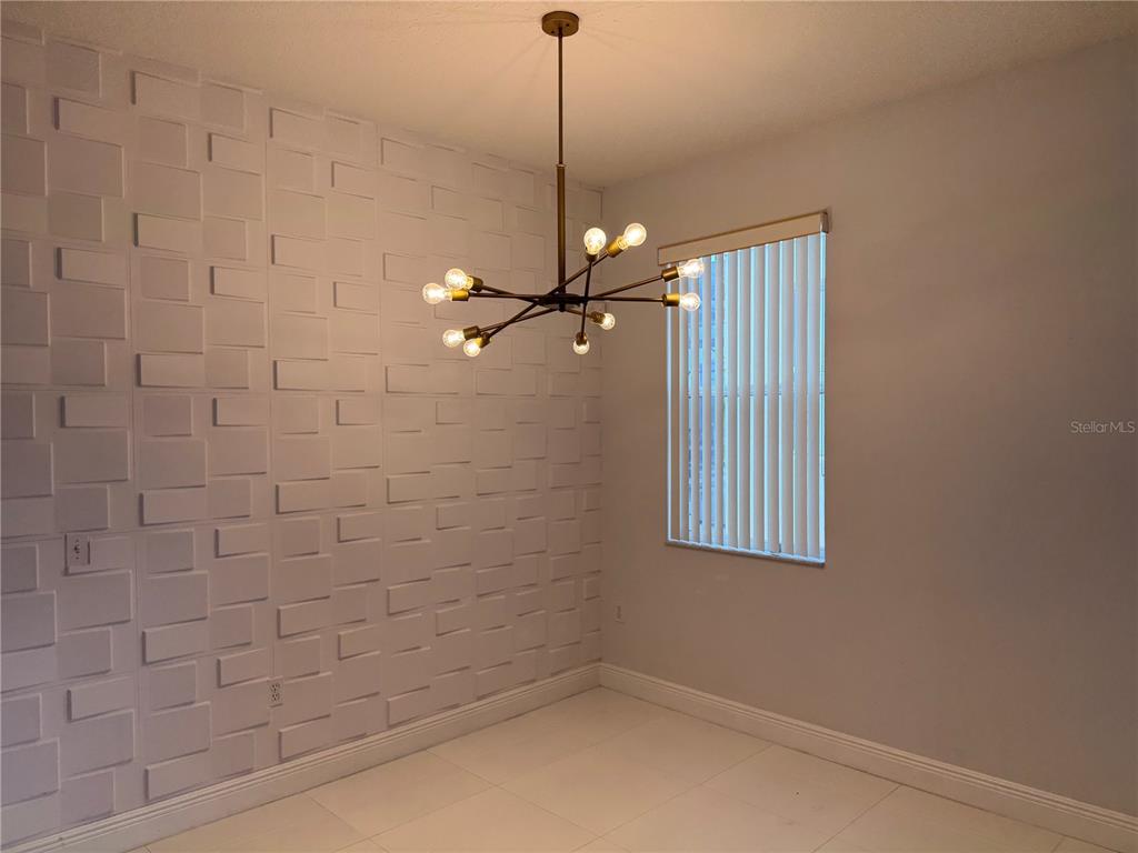A dining room features a textured white accent wall, tile flooring, and a modern chandelier — 1112 PINE RIDGE DRIVE, DAVENPORT, FL