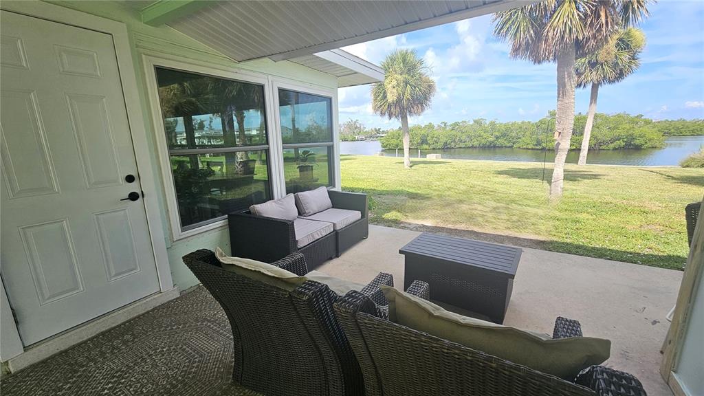 A patio with wicker furniture overlooks a grassy lawn and a body of water — 1210 S MARYKNOLL ROAD, ENGLEWOOD, FL