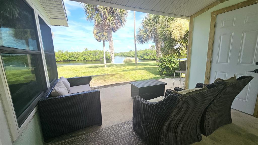 A covered patio features wicker furniture and a view of a grassy yard and water — 1210 S MARYKNOLL ROAD, ENGLEWOOD, FL
