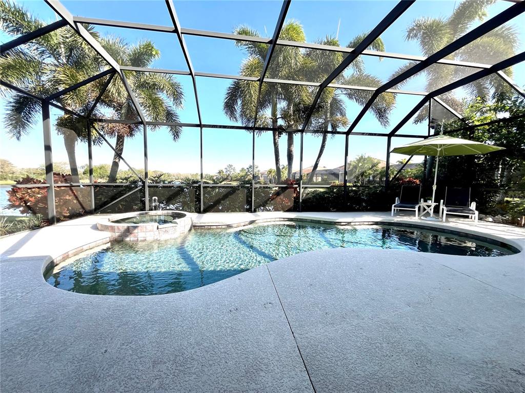A screened-in pool area features a spa, patio furniture, and palm trees in the background — 7709 RIVER PRESERVE DRIVE, BRADENTON, FL