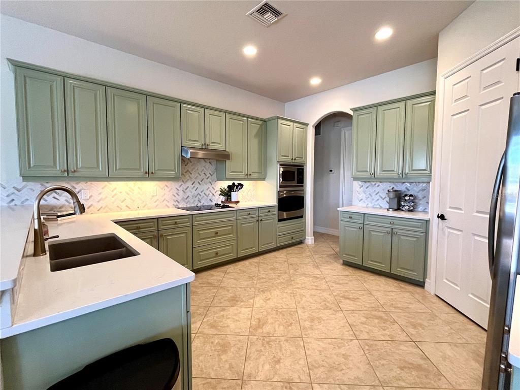 A kitchen features sage green cabinets, white countertops, a herringbone backsplash, and tile flooring — 7709 RIVER PRESERVE DRIVE, BRADENTON, FL