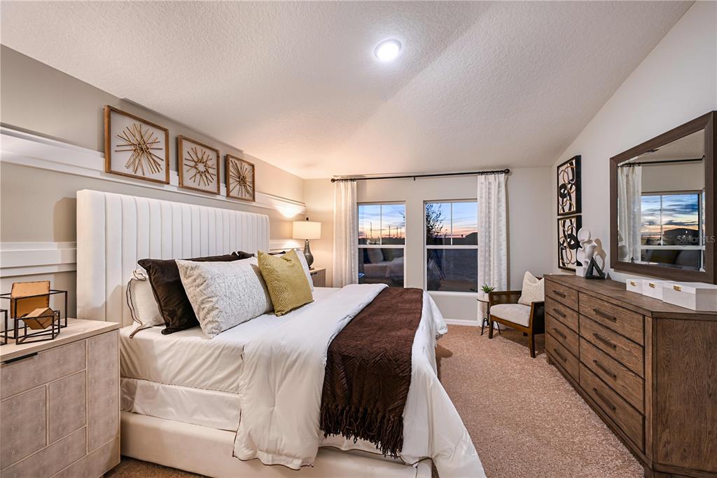 A bedroom features a white tufted headboard, a wooden dresser, and two windows at sunset — 1815 POPPY DRIVE, LAKE HAMILTON, FL
