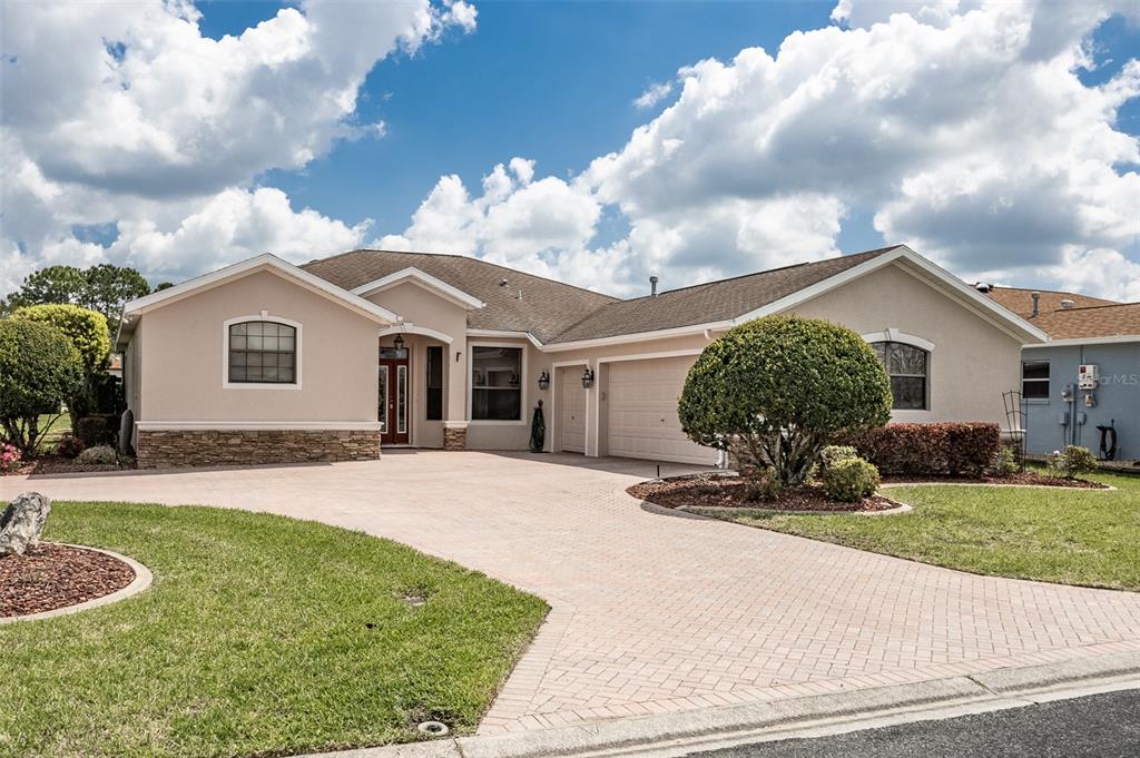 A single-story house with a beige stucco exterior, stone accents, and a paved driveway — 15681 SW 16TH TERRACE, OCALA, FL