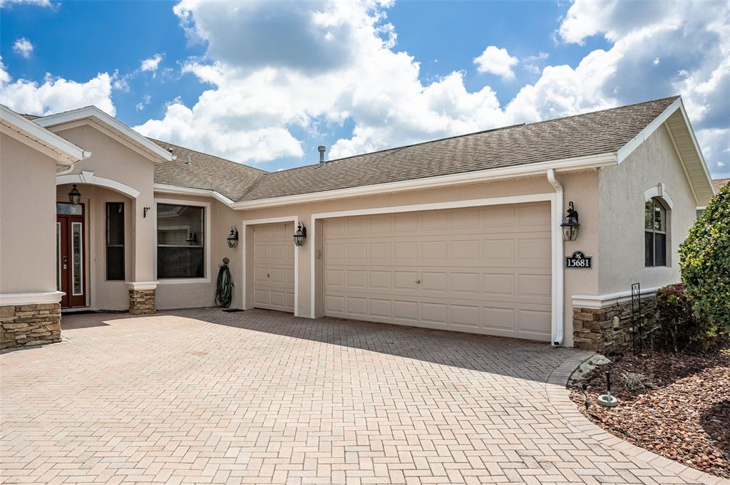 A beige house exterior features a paved driveway, a three-car garage, and stone accents — 15681 SW 16TH TERRACE, OCALA, FL