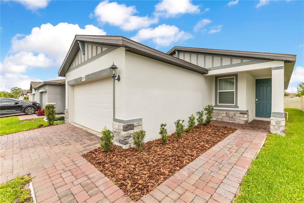 A single-story house exterior features a two-car garage, stone accents, and a paved walkway — 1831 CARNOSTIE ROAD, WINTER HAVEN, FL
