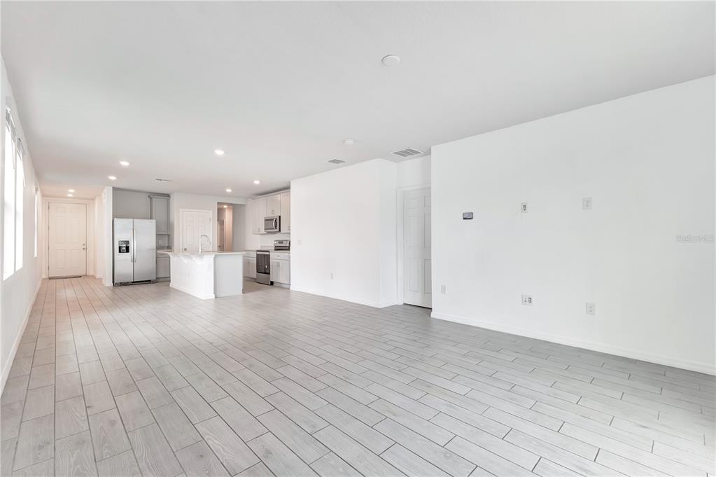 An open-concept living area features white walls, light-colored wood-look tile flooring, and a modern kitchen — 1831 CARNOSTIE ROAD, WINTER HAVEN, FL
