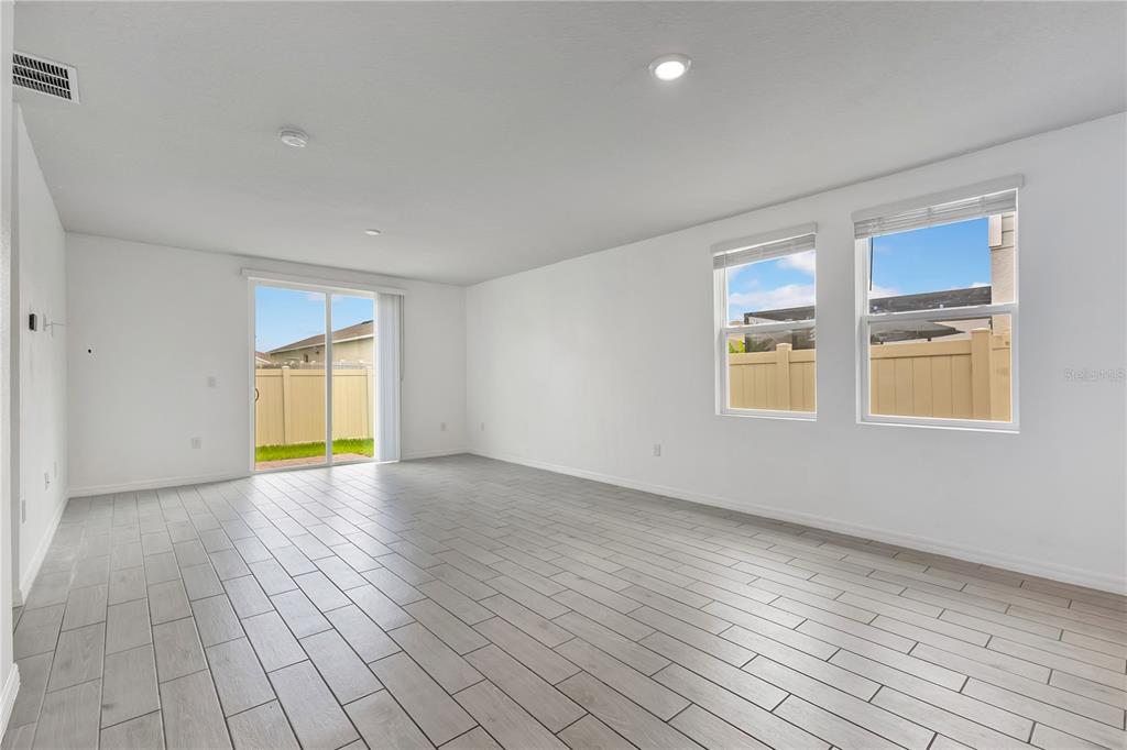 An empty living room features light gray tile flooring, white walls, and a sliding glass door — 1831 CARNOSTIE ROAD, WINTER HAVEN, FL