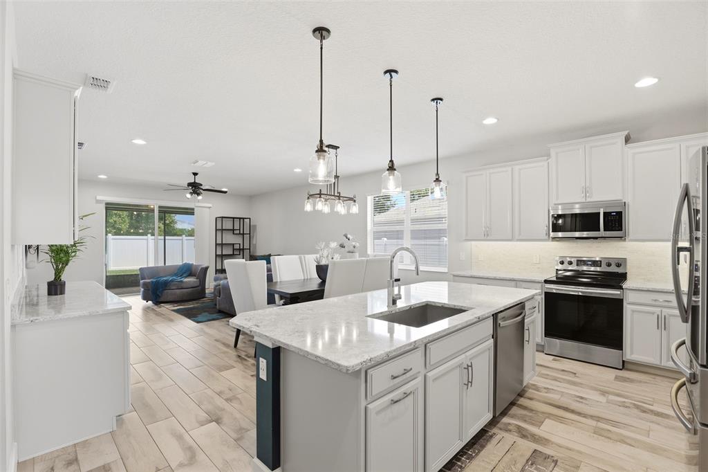 A kitchen with white cabinets, granite countertops, and a center island opens to a dining area — 832 JETWAY STREET, ORANGE CITY, FL