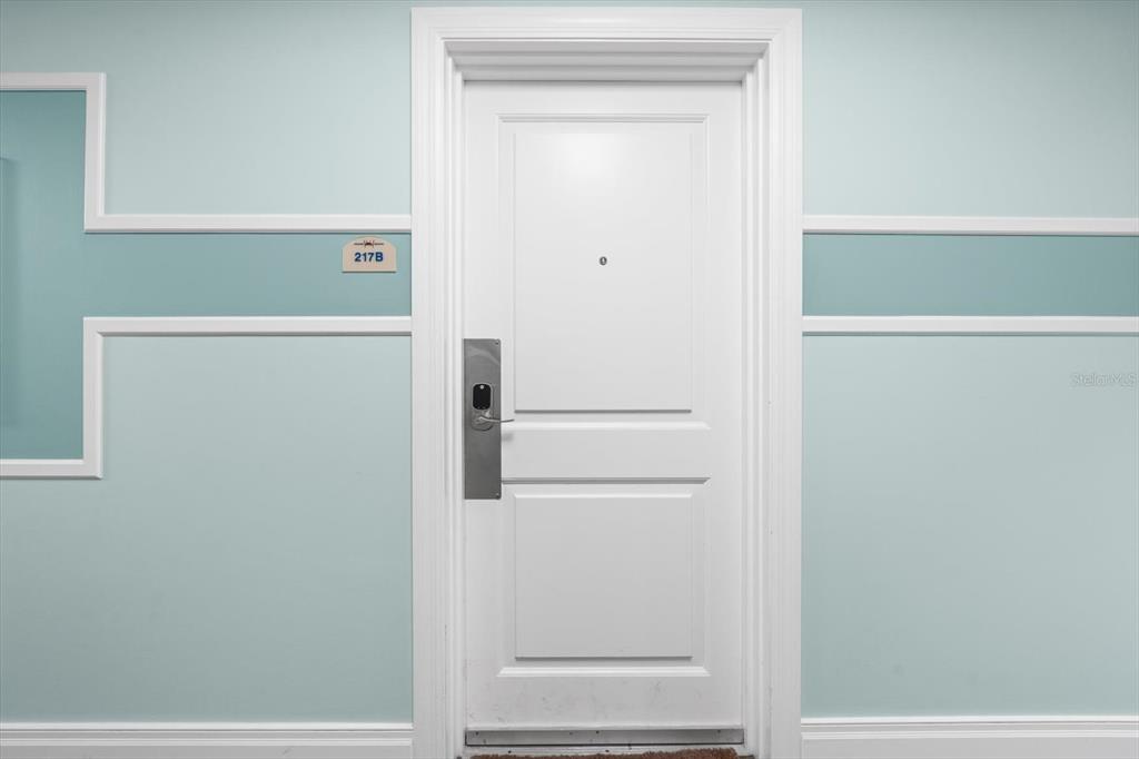 A white door with a keyless entry lock is centered on a light blue wall — 536 BAHIA BEACH BOULEVARD UNIT 311A, RUSKIN, FL