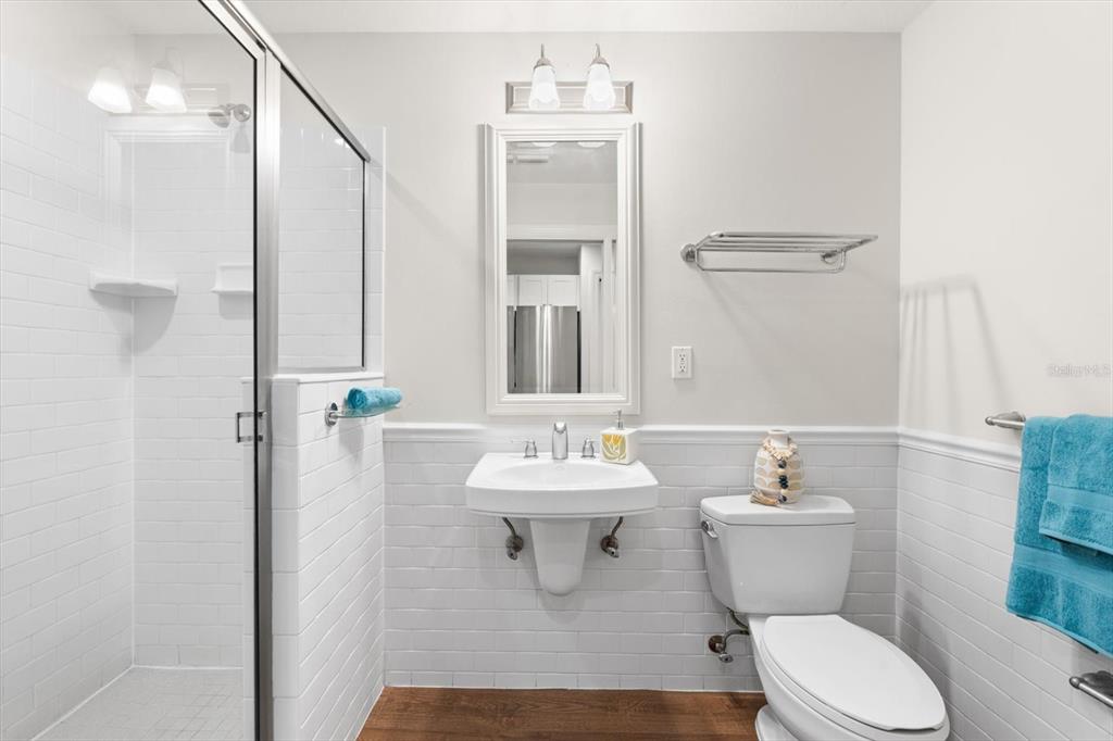 A bathroom features a wall-mounted sink, a glass-enclosed shower, and white subway tile wainscoting — 536 BAHIA BEACH BOULEVARD UNIT 311A, RUSKIN, FL