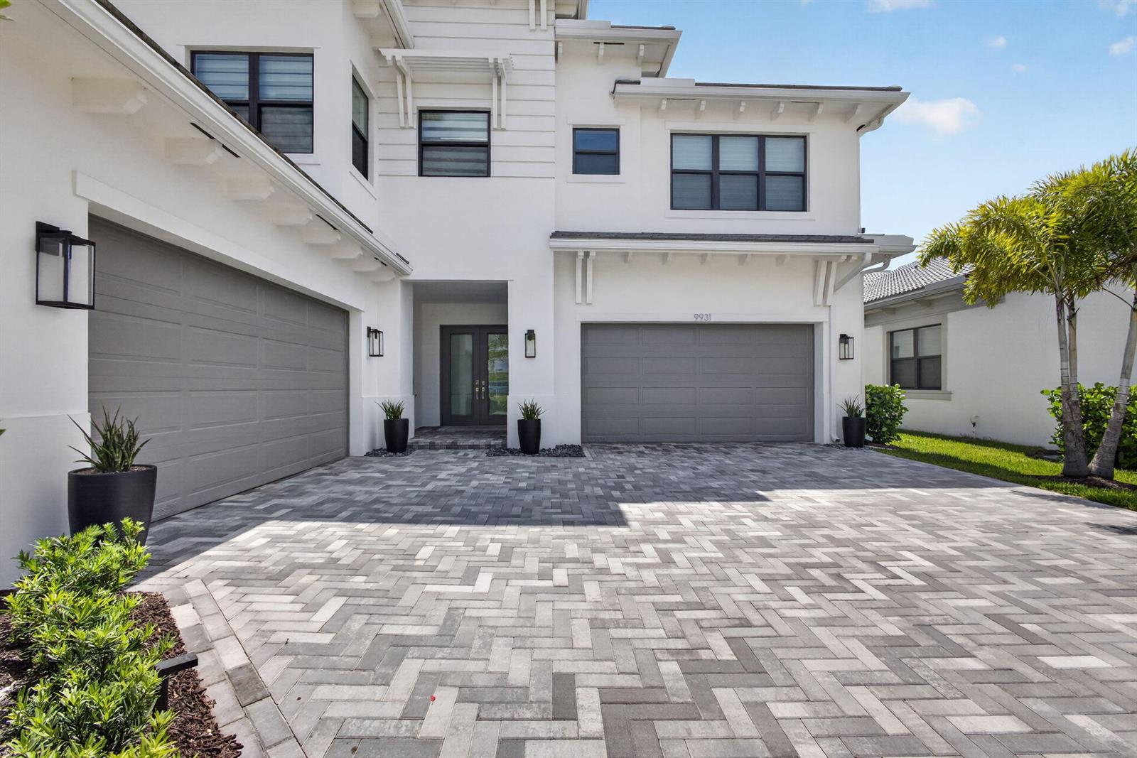 A two-story white house features a gray paver driveway, two garage doors, and landscaping — 9931 Migration Point, Palm Beach Gardens FL 33412, PALM BEACH GARDENS, FL