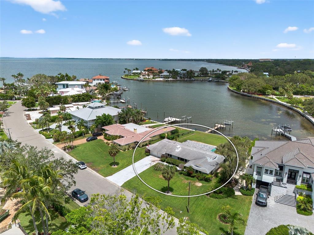 An aerial view shows a single-story house with a screened pool enclosure near the water — 377 S SHORE DRIVE, SARASOTA, FL
