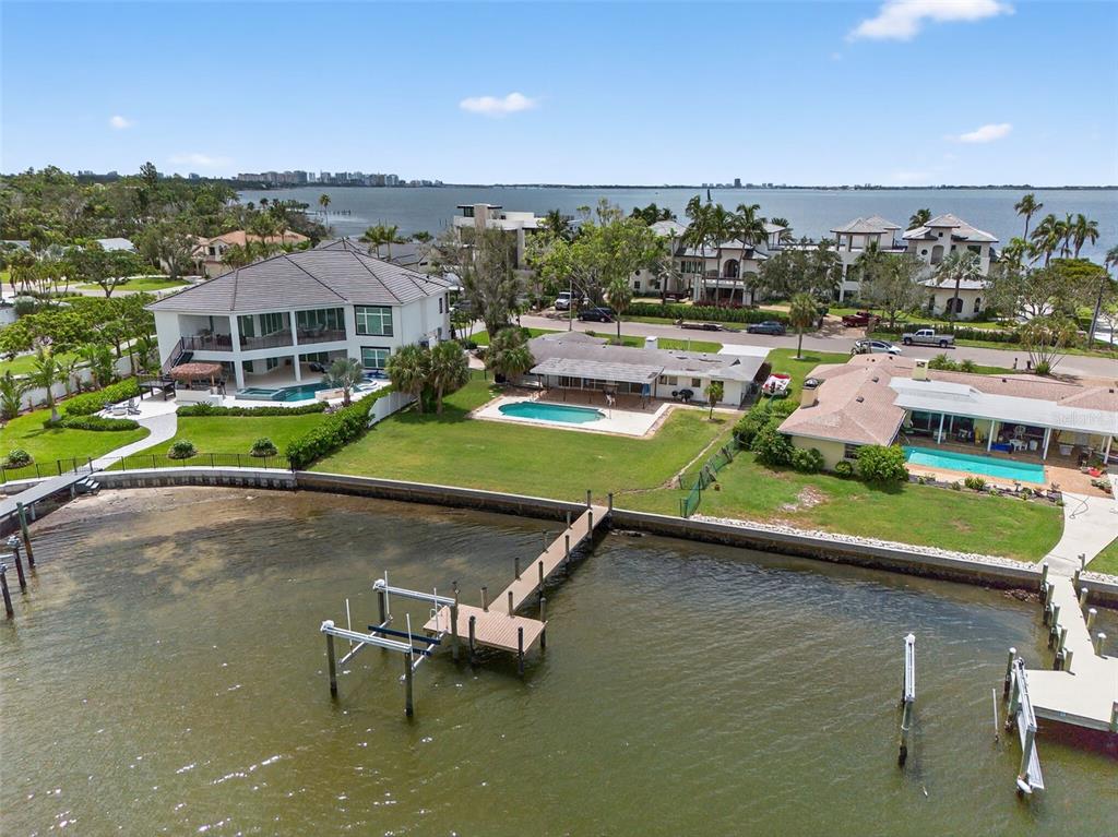 An aerial view shows three waterfront houses with swimming pools and a shared wooden dock — 377 S SHORE DRIVE, SARASOTA, FL