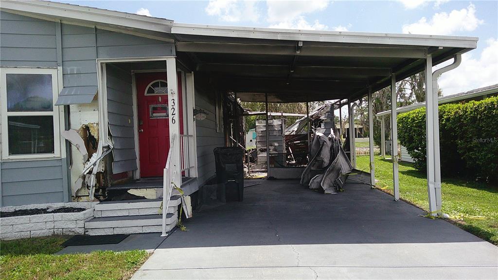 A damaged mobile home exterior features a red front door and a collapsed metal carport — 6710 36TH AVENUE E UNIT 326, PALMETTO, FL