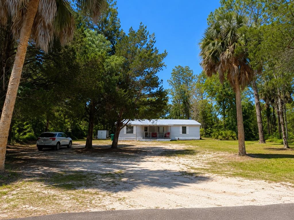 A white single-story house sits on a sandy lot surrounded by trees and palm trees — 8588 W WINGS LANE, CRYSTAL RIVER, FL