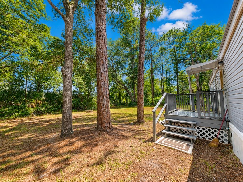 A wooden deck with stairs leads from a mobile home into a wooded backyard — 8588 W WINGS LANE, CRYSTAL RIVER, FL