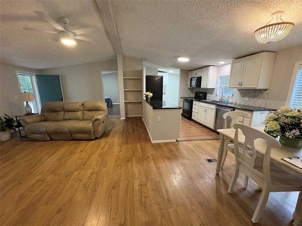 An open-concept living room and kitchen featuring wood-look flooring, white cabinets, and a beige sofa — 8588 W WINGS LANE, CRYSTAL RIVER, FL