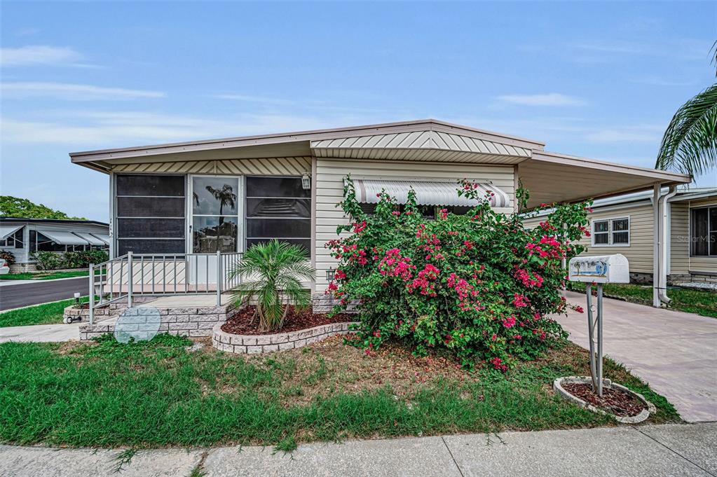A single-story manufactured home features light siding, a screened-in porch, and a large bougainvillea bush — 10539 TAHITIAN LANE UNIT 112, LARGO, FL