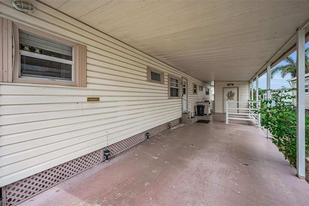 A covered concrete carport runs alongside the exterior wall of a light-colored mobile home — 10539 TAHITIAN LANE UNIT 112, LARGO, FL