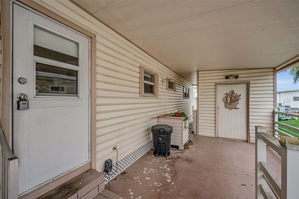 A covered porch with light-colored siding, two white doors, and a black trash can — 10539 TAHITIAN LANE UNIT 112, LARGO, FL
