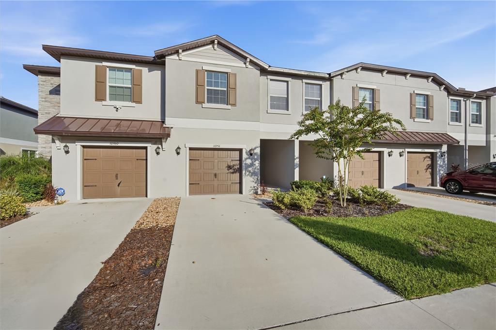 A row of two-story townhomes with beige stucco facades, brown garage doors, and concrete driveways — 10956 WISHING CLOUD ROAD, LAND O LAKES, FL