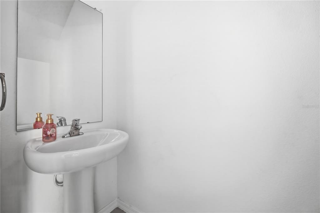 A white pedestal sink with a chrome faucet sits below a rectangular wall mirror — 10956 WISHING CLOUD ROAD, LAND O LAKES, FL