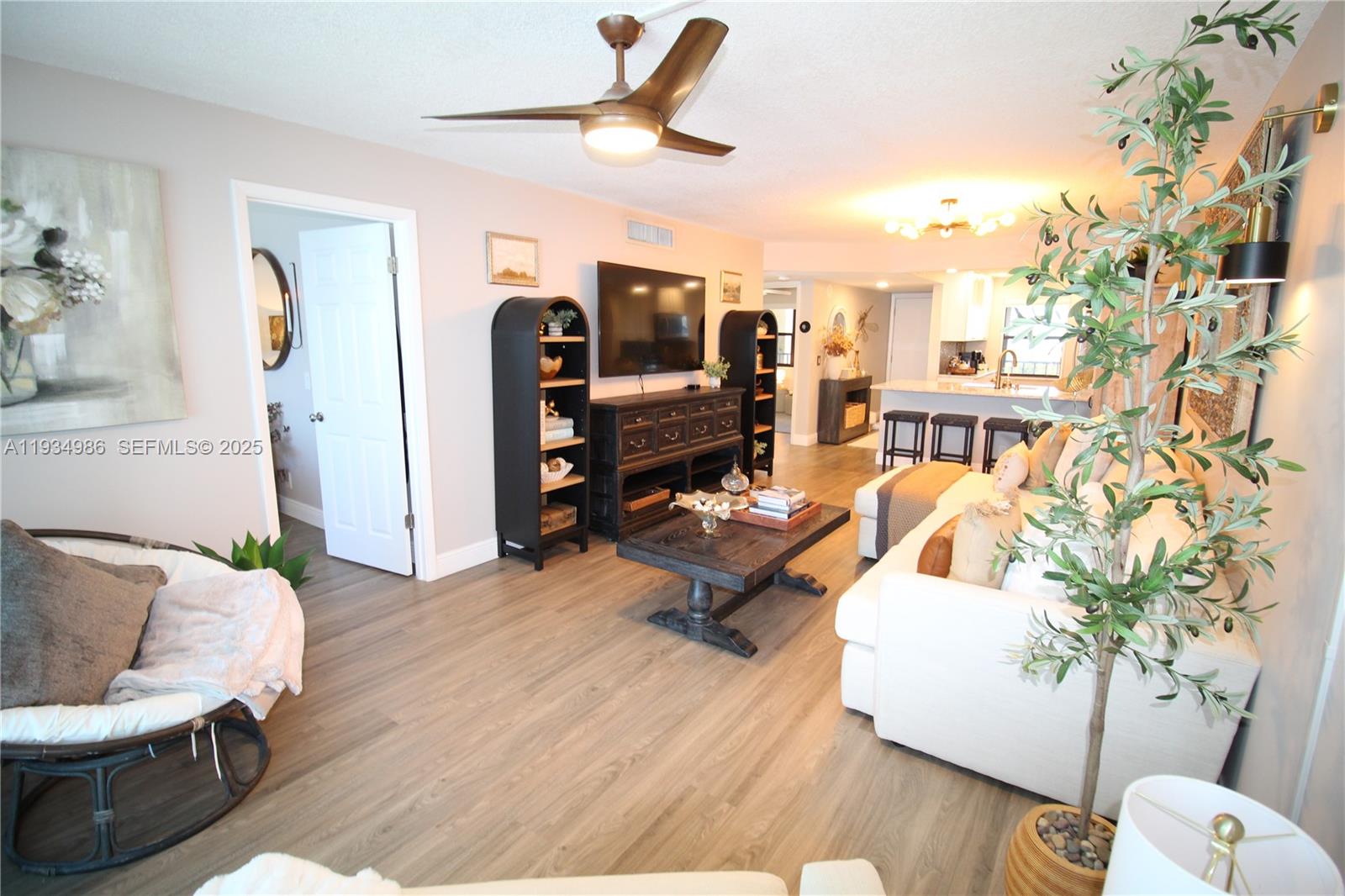 A living room features wood-look flooring, a ceiling fan, a television, and an open kitchen — 7370 S Ocean Dr # 715, Jensen Beach FL 34957, JENSEN BEACH, FL