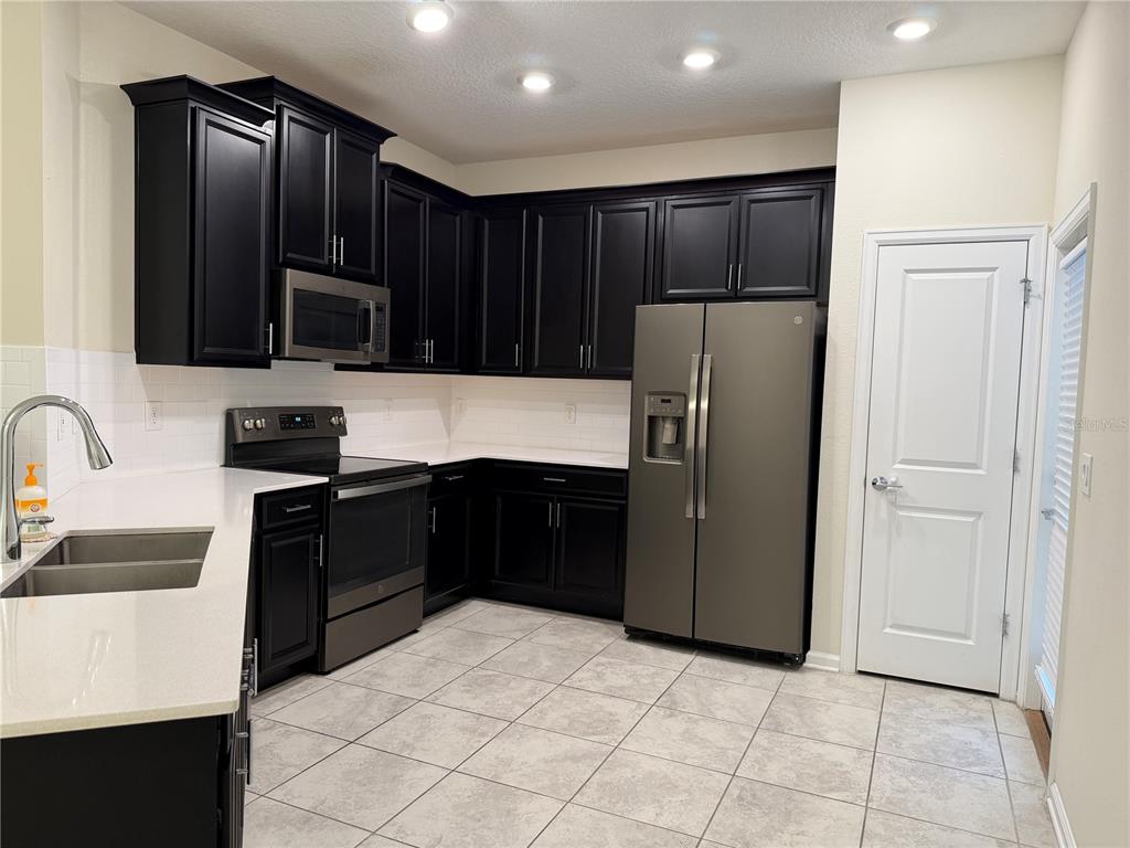A kitchen features black cabinets, stainless steel appliances, white countertops, and light-colored tile flooring — 8513 GOLF WAY, DAVENPORT, FL