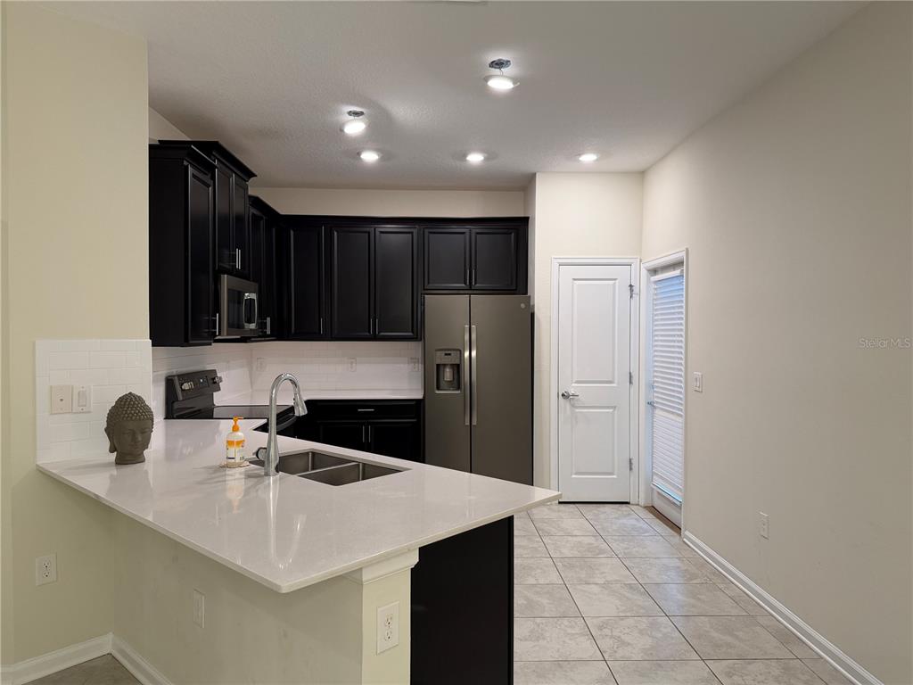 A kitchen features black cabinets, white countertops, stainless steel appliances, and light tile flooring — 8513 GOLF WAY, DAVENPORT, FL