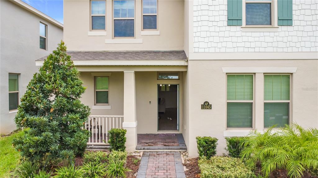 A two-story house exterior features a covered front porch, brick walkway, and green shutters — 11045 BOSTWICK ALLEY, WINTER GARDEN, FL